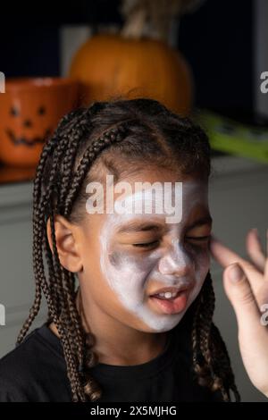 Primo piano di una donna che applica la pittura sulla faccia dei figli per Halloween Foto Stock