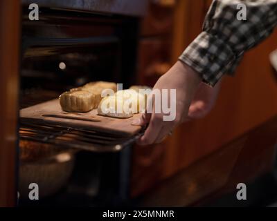 Donna che mette le torte lunari in forno Foto Stock