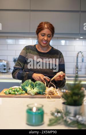 Donna sorridente che sbuccia la radice di prezzemolo in cucina Foto Stock