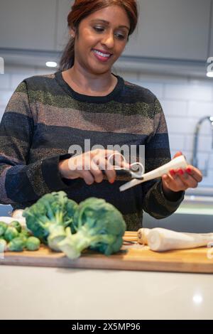 Donna sorridente che sbuccia la radice di prezzemolo in cucina Foto Stock