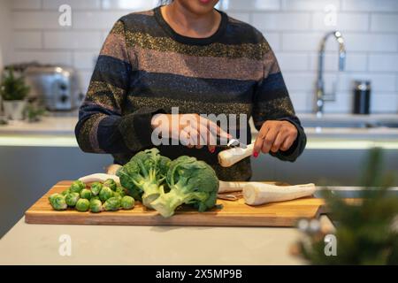 Sezione intermedia di donna che sbuccia la radice di prezzemolo in cucina Foto Stock