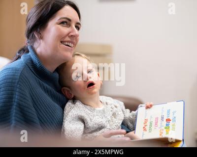 Figlio seduto in grembo alla madre e con un libro in mano Foto Stock