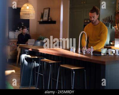 Uomo che lava i piatti mentre fidanzato usa un tablet digitale nella cucina di casa Foto Stock