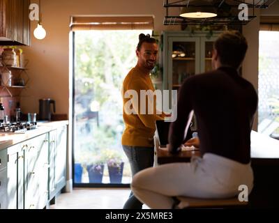 Uomo che lava i piatti mentre fidanzato usa un tablet digitale nella cucina di casa Foto Stock