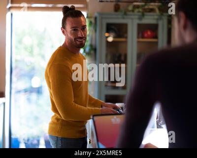 Uomo che lava i piatti mentre fidanzato usa un tablet digitale nella cucina di casa Foto Stock