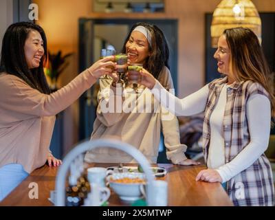 Amiche che fanno un brindisi celebrativo in cucina Foto Stock