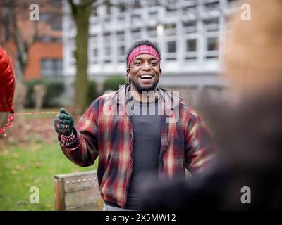 Uomo sorridente con palloncino a forma di cuore che saluta fidanzata Foto Stock