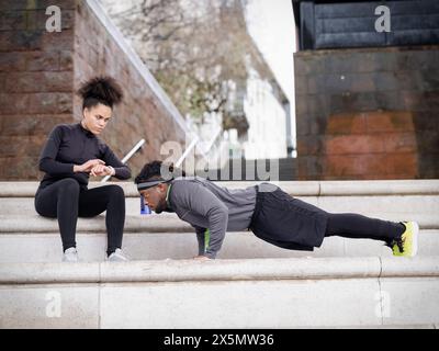 Donna atletica che assiste l'uomo a fare push-up sui gradini all'aperto Foto Stock