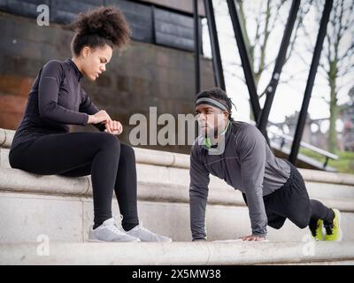 Donna atletica che assiste l'uomo a fare push-up sui gradini all'aperto Foto Stock