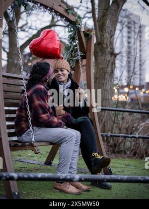 Coppia sorridente con palloncino a forma di cuore seduto sull'altalena Foto Stock