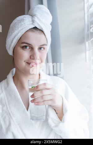 Ritratto di donna in accappatoio e asciugamano turbante con bicchiere d'acqua Foto Stock