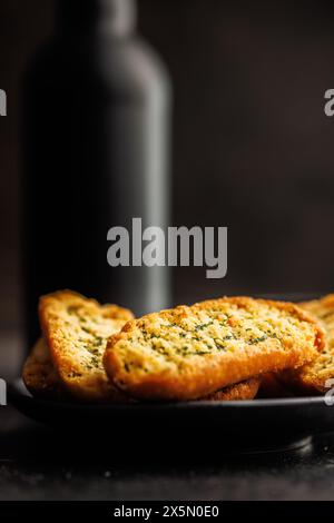 Fette di pane croccanti all'aglio ricoperte di erbe su un tavolo nero. Foto Stock