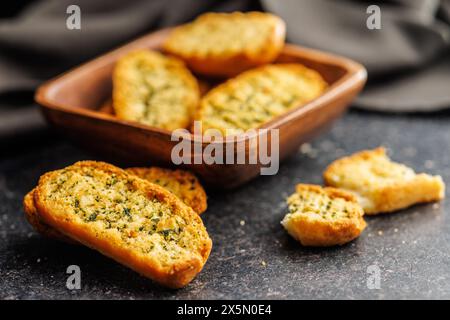 Fette di pane croccanti all'aglio ricoperte di erbe su un tavolo nero. Foto Stock