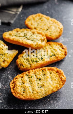 Fette di pane croccanti all'aglio ricoperte di erbe su un tavolo nero. Foto Stock