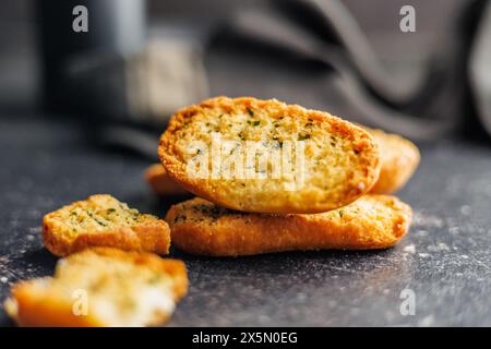 Fette di pane croccanti all'aglio ricoperte di erbe su un tavolo nero. Foto Stock