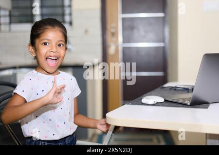 Una giovane ragazza si occupa della sua ergonomia regolando il suo supporto per laptop in una cucina soleggiata. Foto Stock