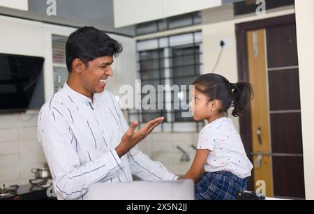 Una ragazza dagli occhi luminosi è affascinata dallo schermo di un notebook in cucina, con il padre che la guida. Foto Stock