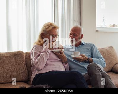 Felice coppia anziana seduto sul divano nel soggiorno e bevendo un caffè Foto Stock