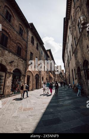 Turisti che camminano lungo una strada trafficata nel centro della storica città medievale di San Gimignano in Toscana, Italia, in una bella giornata di sole. Foto Stock