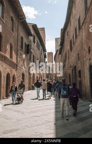 Turisti che camminano lungo una strada trafficata nel centro della storica città medievale di San Gimignano in Toscana, Italia, in una bella giornata di sole. Foto Stock