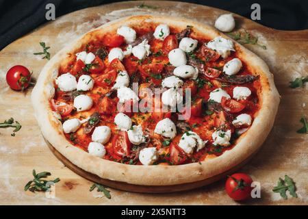 Pizza Margherita appena sfornata con pomodori ciliegini e mozzarella su tavola di legno Foto Stock