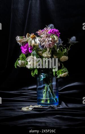 Cattura l'essenza della transitorietà: I fiori induriti si stagliano con grazia in un sereno vaso blu, evocando un senso di nostalgia poetica sullo sfondo Foto Stock