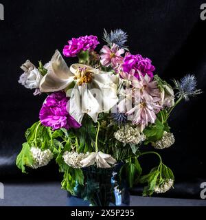 Una delicata disposizione di vecchi fiori selvaggi in un suggestivo vaso blu contrasta splendidamente con il profondo sfondo nero, simboleggiando il passaggio Foto Stock