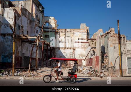 Il pedalò passa per un edificio crollato nel centro di Havana, Cuba Foto Stock