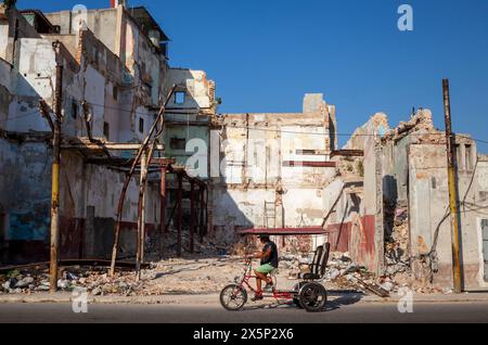 Il pedalò passa per un edificio crollato nel centro di Havana, Cuba Foto Stock