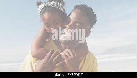 Padre afroamericano che tiene in braccio una figlia, entrambi sorridenti in spiaggia Foto Stock