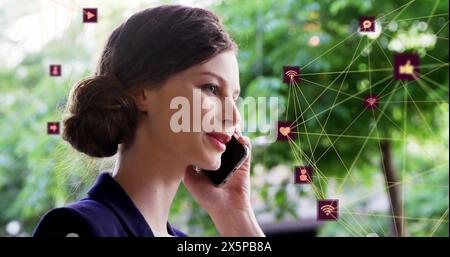 Immagine di icone connesse che formano globi sopra una donna caucasica sorridente che parla al cellulare Foto Stock