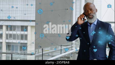 Immagine di icone connesse su un uomo d'affari afroamericano che cammina mentre parla al cellulare Foto Stock