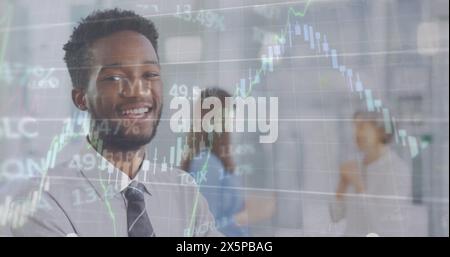 Immagine di grafici, numeri che cambiano, tabellone commerciale, uomo birazziale sorridente in piedi con le braccia incrociate Foto Stock