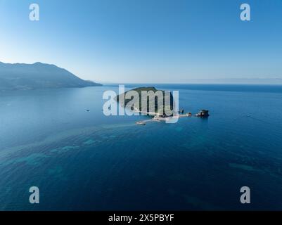 Veduta aerea di Sveti Nicola, isola di Budva, Montenegro. Spiaggia delle Hawaii, ombrelloni e bagnanti e acque cristalline. Coste frastagliate con scogliere a strapiombo Foto Stock