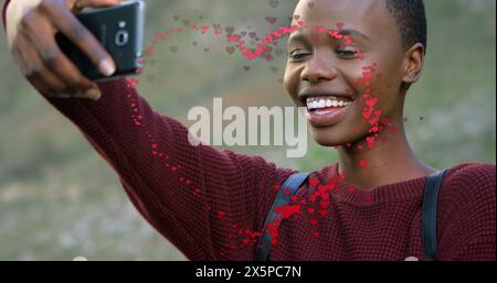 Immagine di cuore su una donna afroamericana felice che sta facendo selfie Foto Stock