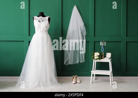 Manichino in abito da sposa e scala a cavalletto con accessori vicino al muro verde Foto Stock