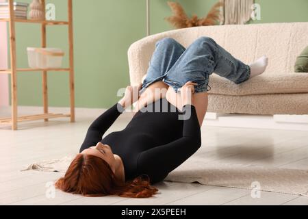 Giovane donna in sovrappeso che cerca di indossare jeans stretti a casa Foto Stock