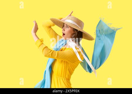 Giovane donna in cappello con vento forte su sfondo giallo Foto Stock