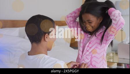 Immagine della luce che si muove sopra la madre e la figlia afroamericana felici che indossano il pigiama Foto Stock