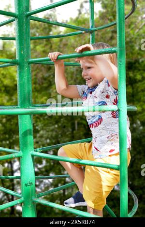 Un bambino sale su una griglia alpina in un parco giochi in una calda giornata estiva. Parco giochi per bambini in un parco pubblico, animazione e ricreazione f Foto Stock