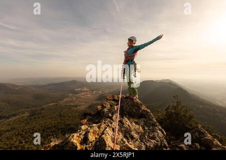 Una donna sta in piedi su una cima di una montagna con una corda attaccata a lei. Indossa un casco e un'imbracatura. Concetto di avventura ed eccitazione, aspetto Foto Stock