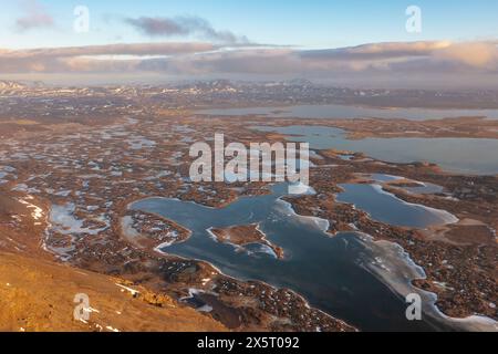 Laghi ghiacciati invernali sulle paludi sulle colline di montagna sotto il nuvoloso tramonto. Islanda, regione nord-orientale Foto Stock