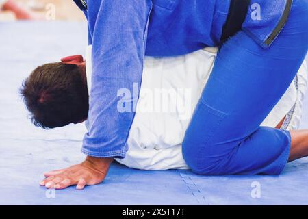 Due uomini su un tappeto blu in una struttura di allenamento brasiliana Jiu-Jitsu. È concentrato e pratica le tecniche dell'arte marziale Foto Stock