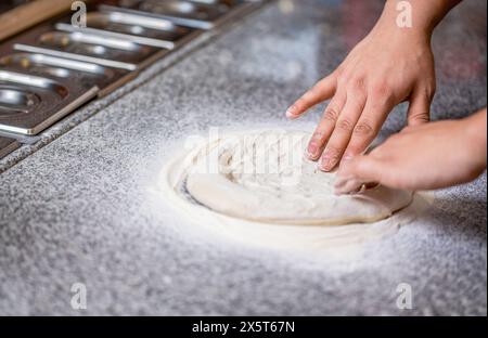 Impastare l'impasto con le mani per preparare la pizza e la farina. Lo chef prepara le mani di impasto per pizza. L'impasto per la pizza viene arrotolato e impastato. Cuocere le mani impastando l'impasto Foto Stock