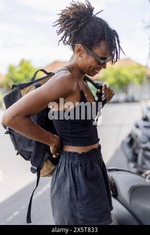 Donna sorridente che indossa lo zaino in strada Foto Stock