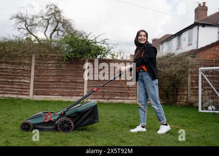 Donna che indossa l'hijab falciando l'erba nel cortile Foto Stock