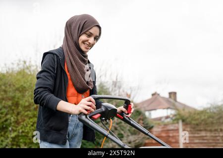 Donna che indossa l'hijab falciando l'erba nel cortile Foto Stock