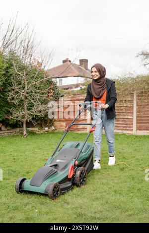 Donna che indossa l'hijab falciando l'erba nel cortile Foto Stock