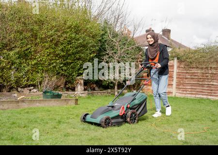 Donna che indossa l'hijab falciando l'erba nel cortile Foto Stock