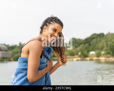 Donna sorridente in piedi avvolta in un asciugamano vicino al lago Foto Stock